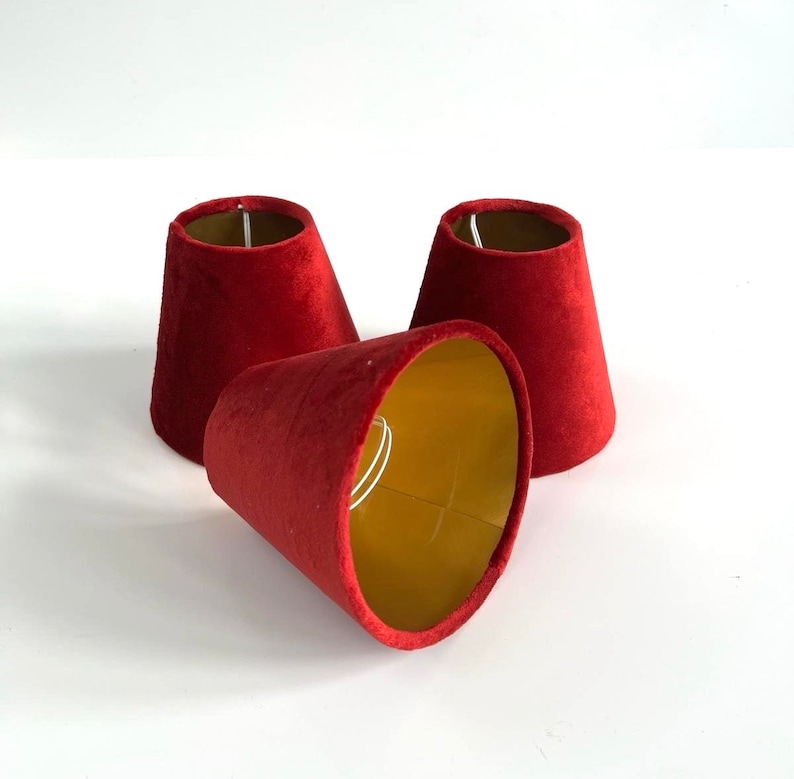 May include: Three red velvet lampshades with gold interiors. The lampshades are cone-shaped and have a simple design.