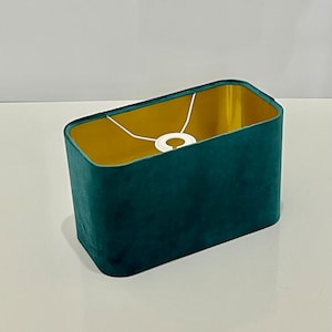 Può includere: Un paralume rettangolare con un esterno in velluto verde acqua e un interno dorato. Il paralume ha un cordoncino bianco per l'appeso.