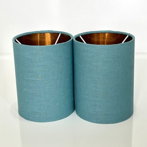 May include: Two light blue lampshades with a copper lining. The lampshades are made of a textured fabric.