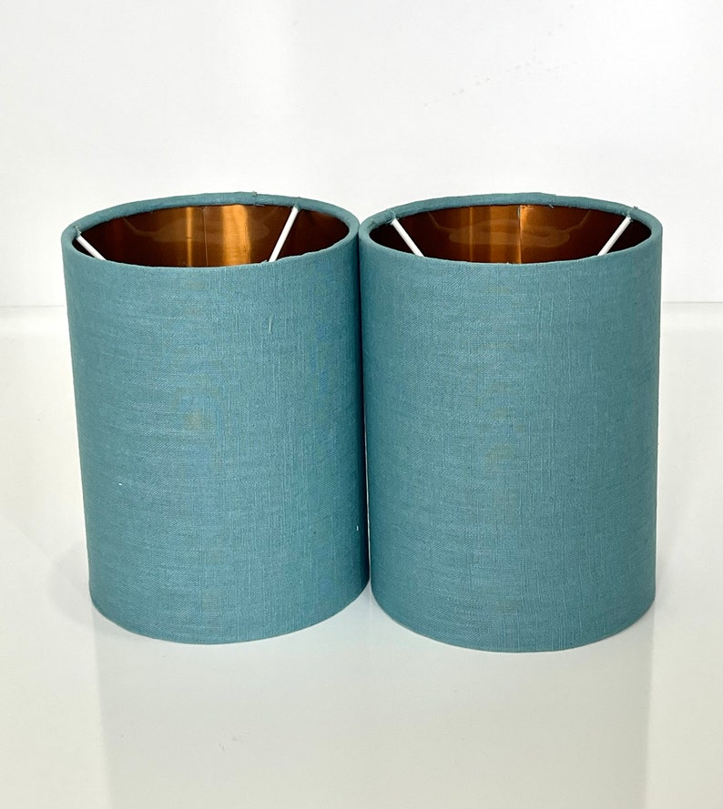 May include: Two light blue lampshades with a copper lining. The lampshades are made of a textured fabric.
