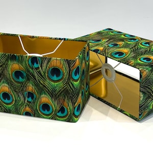 Peut inclure: Deux abat-jours rectangulaires avec un intérieur doré et un motif de plumes de paon. Les abat-jours sont en tissu et ont un cordon blanc.