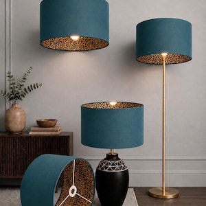 May include: Teal drum lampshades with a leopard print interior are featured in this image. One lampshade is lying on the floor, while others are attached to a pendant light, a floor lamp, and a table lamp. The lampshades are a stylish home decor item.