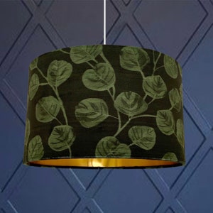 Peut inclure: Un abat-jour vert et or avec un motif de feuilles. L'abat-jour est en tissu et a une bordure dorée.