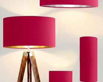 May include: A collection of lighting fixtures featuring vibrant magenta fabric drum shades. The set includes a tripod floor lamp with a wooden base, a tall cylindrical table lamp with a gold base, and a shorter table lamp with a rounded gold base.