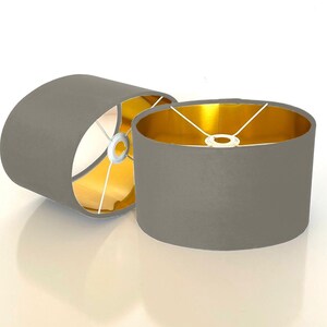 May include: Two gray oval lampshades with gold interiors. The lampshades are made of fabric and have a simple, modern design.