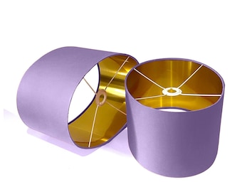 May include: Two oval-shaped lampshades with a purple fabric exterior and a gold interior. The lampshades are made of a soft, luxurious fabric.