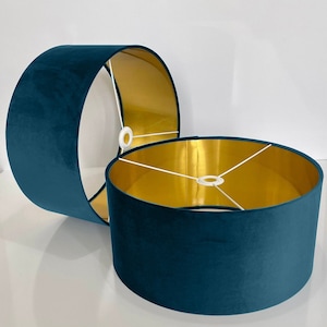 May include: Two teal blue velvet lampshades with gold lining. The lampshades are cylindrical and have a white cord running through the center.