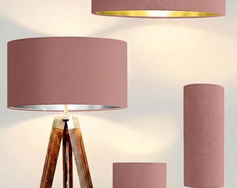 May include: A collection of lighting fixtures featuring dusty rose fabric drum shades. Included are a tripod floor lamp with a wooden base, a pendant light with a gold interior, and two table lamps with gold-toned bases of varying heights.