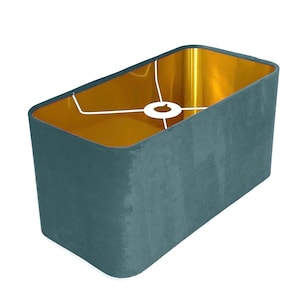 Peut inclure: Un abat-jour rectangulaire avec un extérieur en velours bleu sarcelle et un intérieur doré. L'abat-jour a un anneau métallique blanc pour fixer une ampoule.