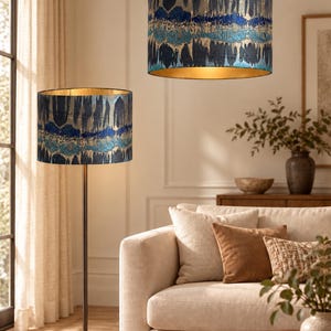 May include: A floor lamp and a matching pendant light, both featuring cylindrical shades with a textured, abstract pattern in shades of deep blue, teal, and gold. The interior of each shade has a metallic gold finish, and the floor lamp has a thin, dark metal stand.