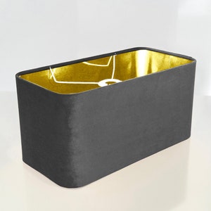 May include: A rectangular lampshade with a dark gray fabric exterior and a gold interior. The lampshade is designed for a standard light bulb.
