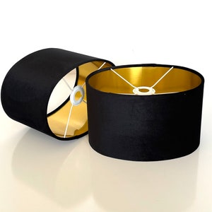 May include: Two black oval lampshades with gold interiors. The lampshades are made of fabric and have a simple design.