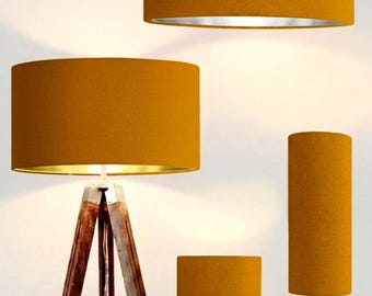 May include: A collection of four lighting fixtures featuring mustard yellow fabric drum shades. Included are one hanging pendant light, one tripod floor lamp with dark wood legs, and two table lamps with metallic bases of varying heights.