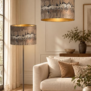 May include: A floor lamp and a matching pendant light, both featuring cylindrical shades with a textured, metallic bronze and black abstract pattern and a reflective gold interior lining. The floor lamp has a slender dark metal stand and base.
