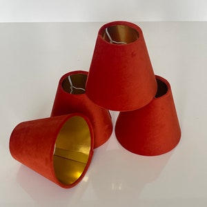 May include: Four red velvet lampshades with gold interiors. The lampshades are stacked on top of each other.