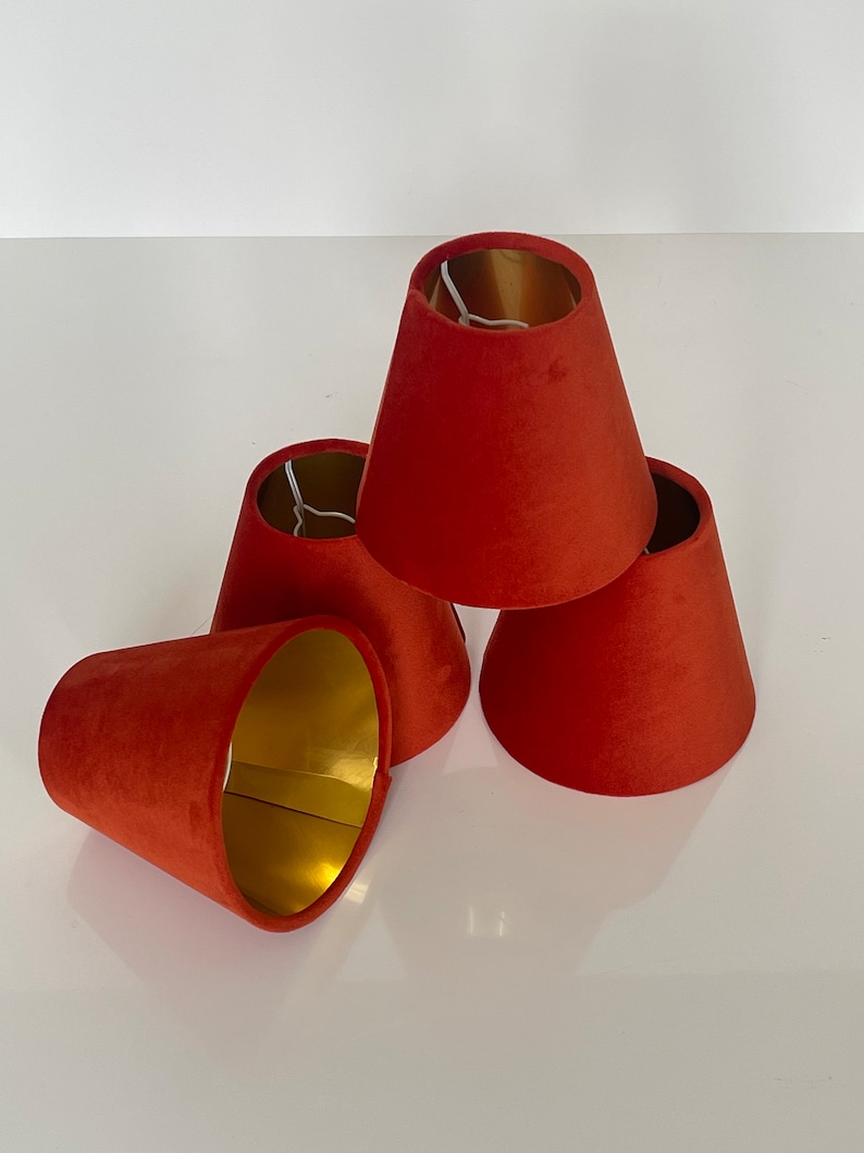 May include: Four red velvet lampshades with gold interiors. The lampshades are stacked on top of each other.