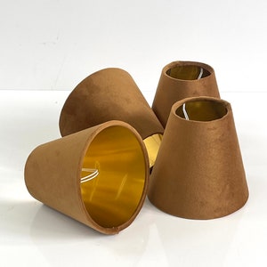 May include: Four brown velvet lampshades with gold lining. The lampshades are cone-shaped and have a smooth texture.