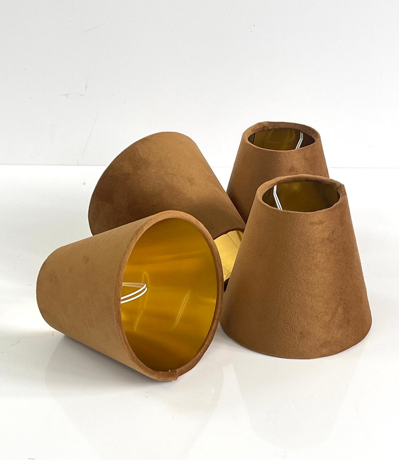 May include: Four brown velvet lampshades with gold lining. The lampshades are cone-shaped and have a smooth texture.