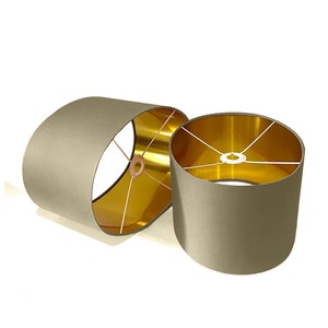 May include: Two oval lampshades with a gold interior. The lampshades are a light gray color.