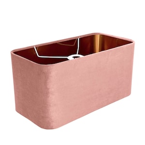 May include: A rectangular lampshade made of dusty rose velvet. The shade has a white cord and a metal ring at the top.