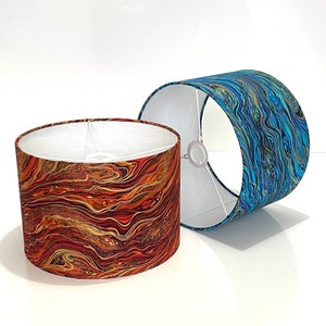 May include: Two lampshades with abstract patterns. One lampshade is red and gold with swirling lines. The other lampshade is blue and green with swirling lines.