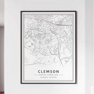 May include: Black and white line art map of Clemson, South Carolina. The map shows the city streets and landmarks. The text "CLEMSON" and "SOUTH CAROLINA" are printed below the map, along with the coordinates "34.6834°N - 82.8374°W".