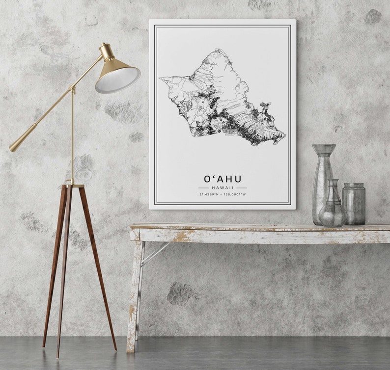 May include: A black and white line art map of Oahu, Hawaii, with the text "O'AHU HAWAII 21.4228&deg;N - 158.0051&deg;W" printed below the map. The map is framed and hanging on a white wall above a whitewashed wooden table.