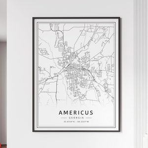 May include: A framed black and white map print of Americus, Georgia. The map shows the city's streets and infrastructure in a minimalist style. The text "Americus Georgia" is centered at the bottom, with the coordinates 32.0724°N - 84.2327°W.