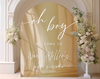 May include: A gold arch with a sheer fabric overlay and the text "oh boy" in white script. The text "Welcome to Noah Miller's Baby Shower 06/07/2024" is also in white.