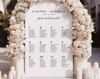 Può includere: Un tableau di posti a sedere per matrimonio bianco con un arco floreale sullo sfondo. Il tableau è intitolato "Harper + Micheal June 07, 2024 your seat awaits!" e elenca i nomi degli ospiti per numero di tavolo.
