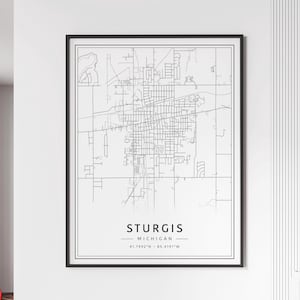 May include: A black framed print featuring a detailed map of Sturgis, Michigan. The map is rendered in black and white, showcasing the city's street layout and landmarks. The text "STURGIS MICHIGAN" is centered at the bottom, with coordinates below.