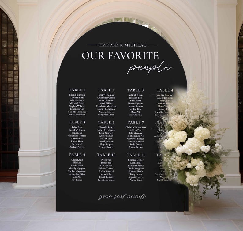 May include: A black archway sign with white text listing table numbers and guest names for a wedding reception. The sign reads "Harper & Micheal Our Favorite People" and includes the phrase "your seat awaits".