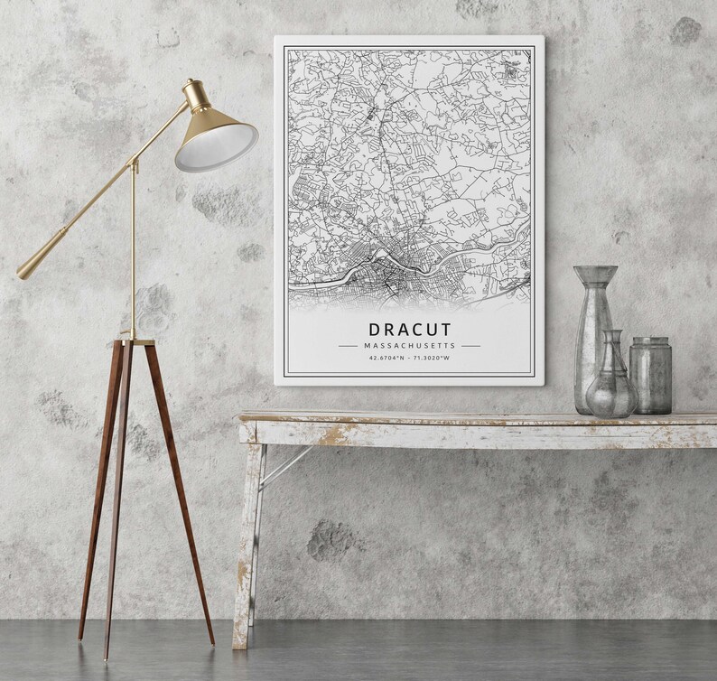 May include: A black and white map print of Dracut, Massachusetts with the city name and coordinates printed at the bottom. The map is framed and hanging on a white wall above a whitewashed wooden shelf with decorative vases.