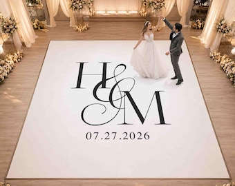 May include: A large square white wedding dance floor featuring a prominent black monogram with the letters H and M intertwined in a decorative serif font, with the date 27.07.2026 printed in black text centred directly below the monogram.