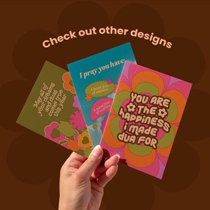 May include: Three greeting cards with floral designs and inspirational messages are held in a hand. The cards have a retro aesthetic with colors like olive green, teal, pink, and orange. Text includes "May all of your dreams and duas come true this year."
