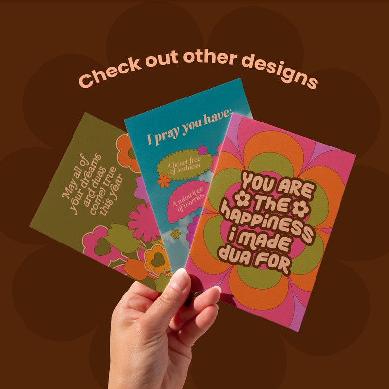 May include: Three greeting cards with floral designs and inspirational messages are held in a hand. The cards have a retro aesthetic with colors like olive green, teal, pink, and orange. Text includes "May all of your dreams and duas come true this year."
