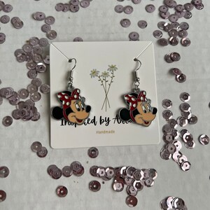 May include: A pair of silver earrings with red and white Minnie Mouse heads. The earrings are on a white card with the text "Inspired by Ava" and "Handmade".