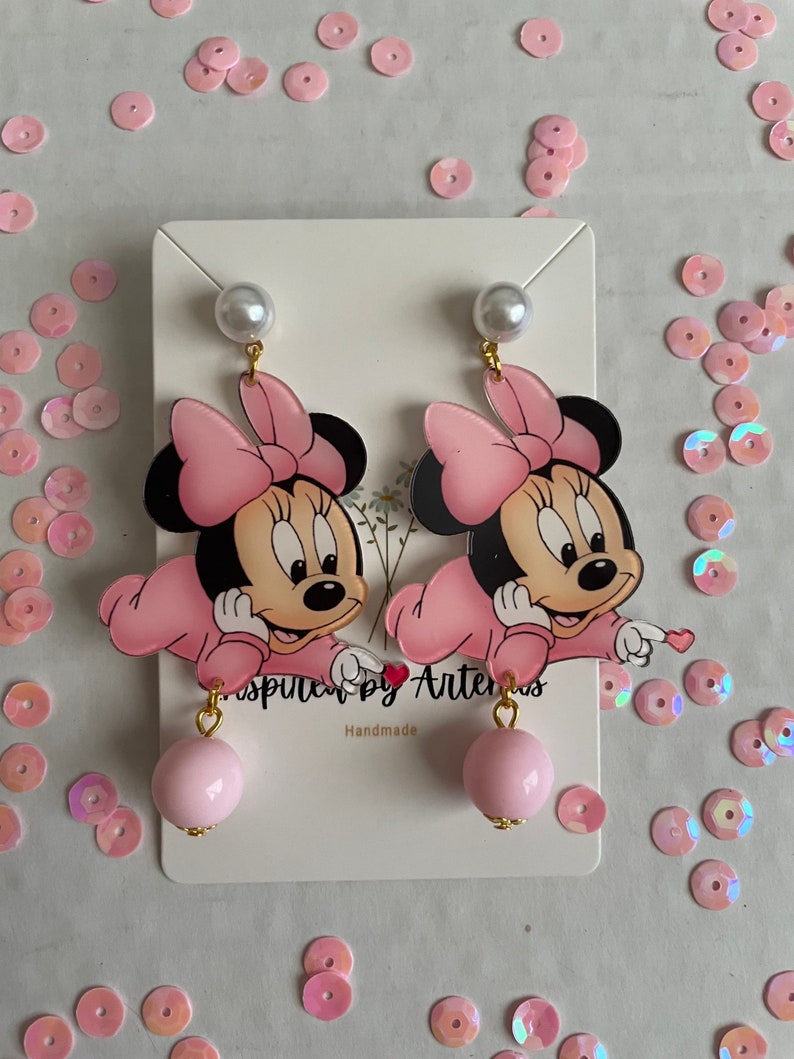 May include: Pink and black Minnie Mouse character earrings with a pink pearl dangle. The earrings are handmade and feature a gold-colored metal.