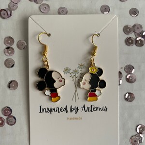 May include: A pair of gold dangle earrings featuring a cartoon couple kissing. The characters are Mickey Mouse and Minnie Mouse. The earrings are handmade and the card reads "Inspired by Artemis".