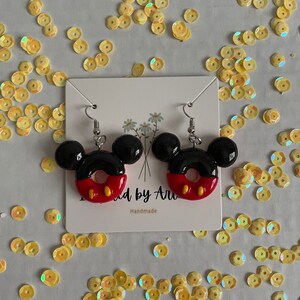 May include: A pair of red, black and yellow Mickey Mouse-shaped earrings. The earrings are shaped like a donut with Mickey Mouse ears on top. The earrings are handmade.