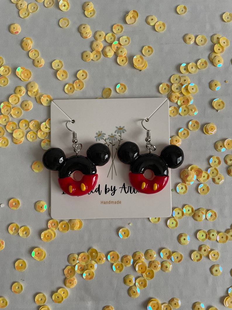 May include: A pair of red, black and yellow Mickey Mouse-shaped earrings. The earrings are shaped like a donut with Mickey Mouse ears on top. The earrings are handmade.