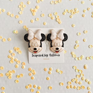 Puede incluir: Un par de pendientes de Minnie Mouse en blanco y negro con detalles de cuentas negras. Los pendientes est&aacute;n hechos a mano y llevan el texto "Inspired by Artemis" y "Handmade".