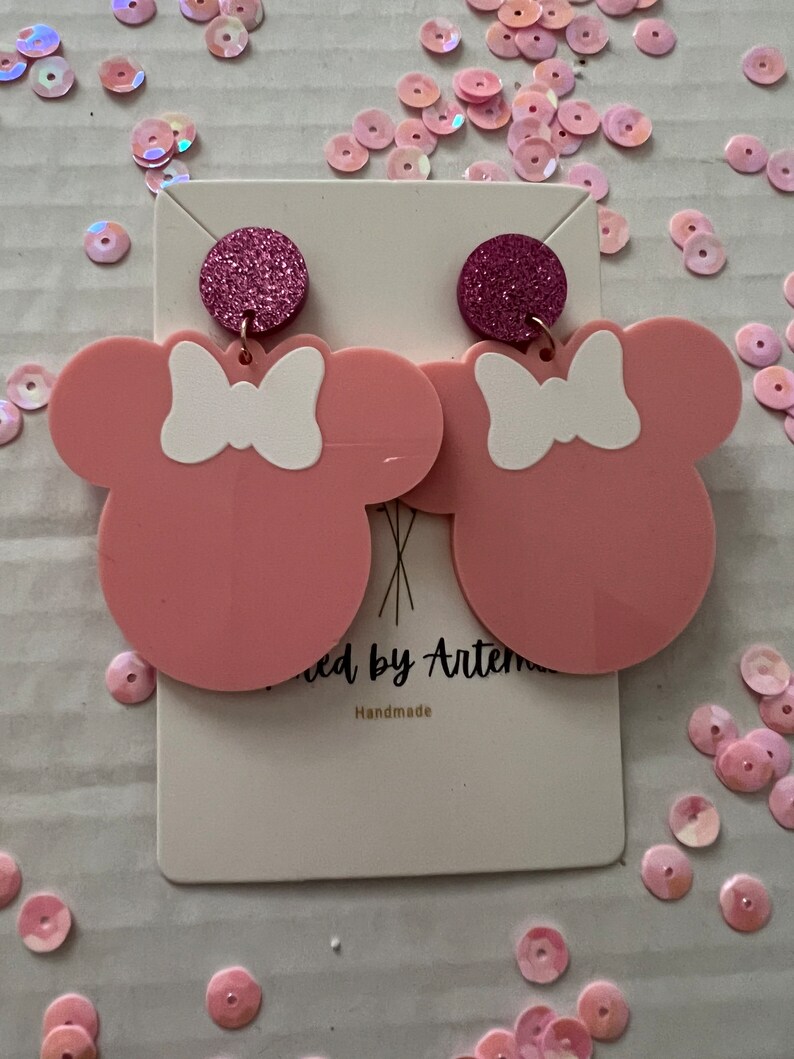 Puede incluir: Pendientes de rat&oacute;n de color rosa y blanco con un acento de purpurina rosa. Los pendientes est&aacute;n hechos a mano y se muestran en una tarjeta blanca con el texto "Made by Artem Handmade".