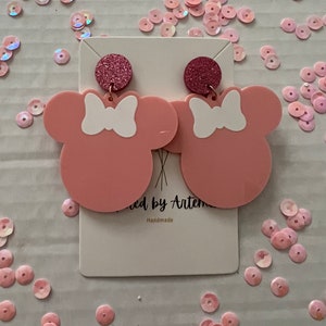 Puede incluir: Pendientes de color rosa en forma de Minnie Mouse con lazos blancos y detalles de purpurina. Hecho a mano.