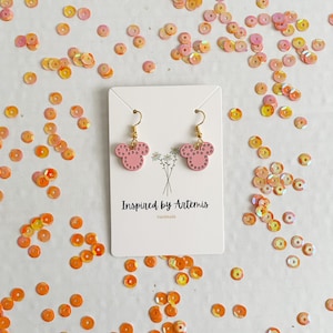 May include: Pink mouse-shaped earrings with gold hooks and white polka dots. The earrings are on a white card with the text "Inspired by Artemis Handmade".