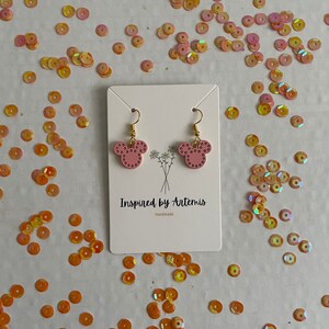May include: Pink mouse-shaped earrings with gold hooks and white polka dots. The earrings are on a white card with the text "Inspired by Artemis Handmade".