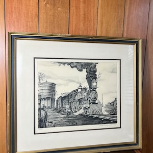 May include: A black and white framed print of a vintage steam locomotive pulling a train. The locomotive is in the foreground and the train is in the background. The print is set against a white background.