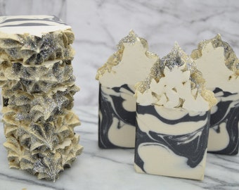 May include: Three bars of handmade soap with a black and white marbled design. The soap is topped with a decorative swirl of white soap and silver glitter.