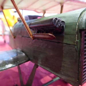 May include: A close-up of a wooden model aeroplane with a green and brown paint scheme. The model has a detailed engine and a propeller.