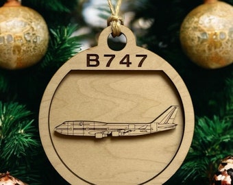 Könnte beinhalten: Ein runder Weihnachtsbaumschmuck aus Holz mit einer Silhouette eines Boeing 747 Flugzeugs im Inneren. Der Schmuck ist braun und trägt den Text "B747" und "Boeing 747".